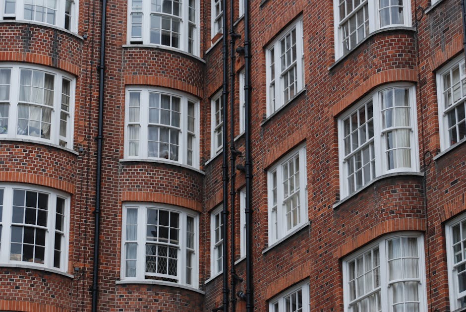 A close-up view of the upper floors of a historic brick building featuring five arched windows with white frames and decorative iron railings. The building's façade is constructed from dark brown bri